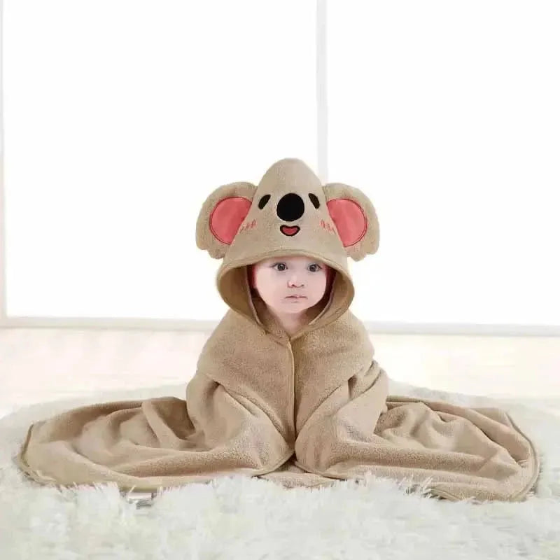 Bébé assis sur tapis moelleux, enveloppé dans une cape à capuche koala beige